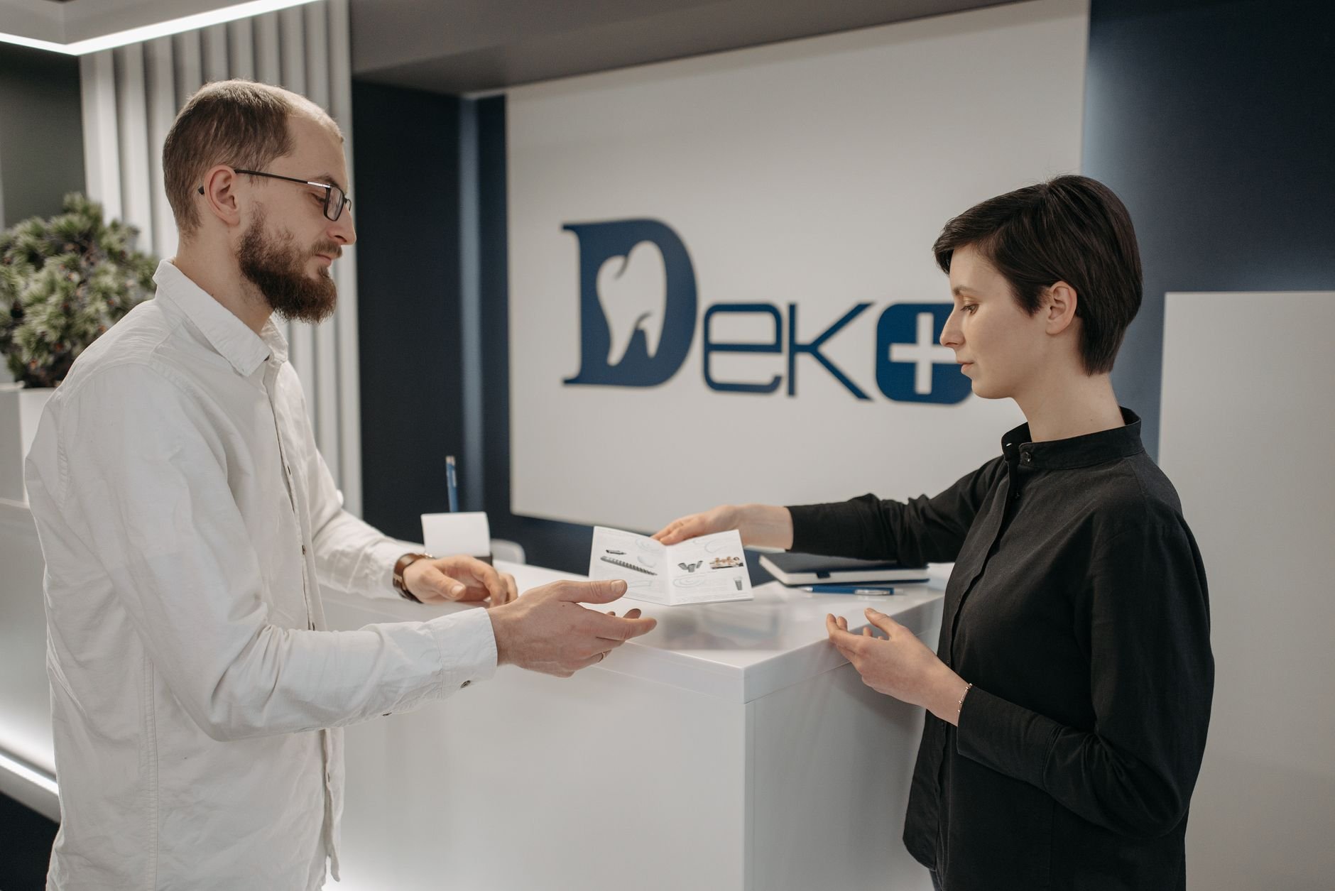 Man and woman exchanging paperwork at a modern dental clinic front desk.